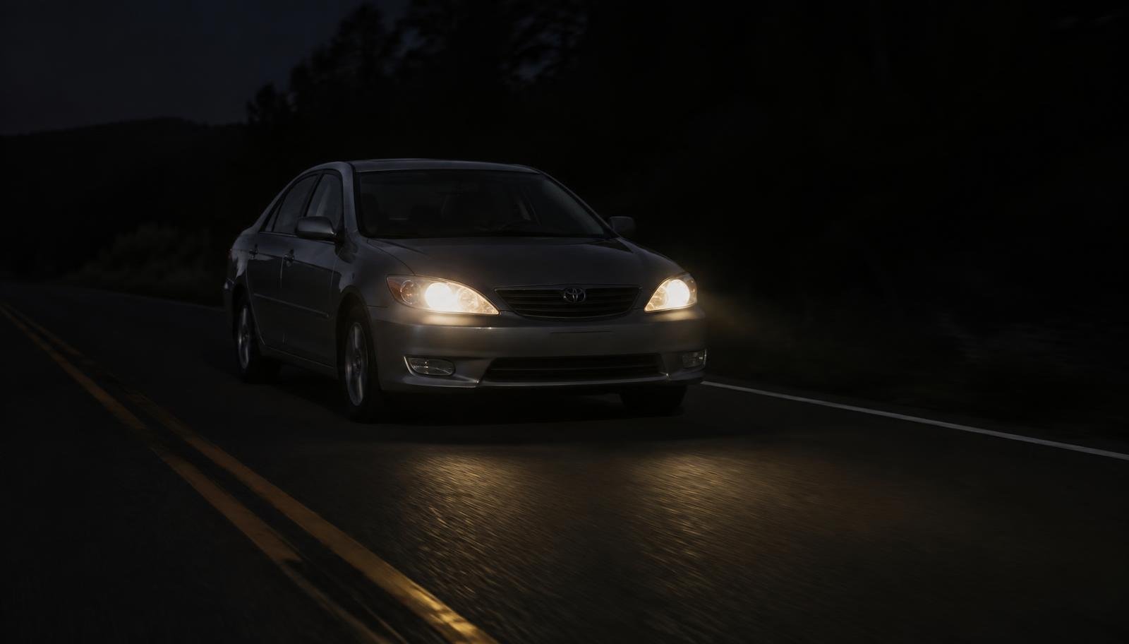 Carro dirigindo à noite em rodovia escura com a luz fraca dos faróis halógenos
